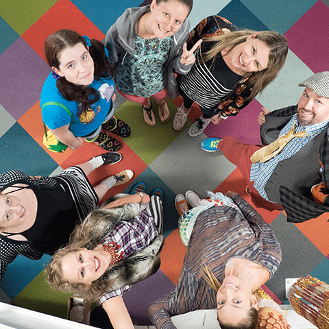 Group of people standing on multi colored carpet in a circle staring up at the camera