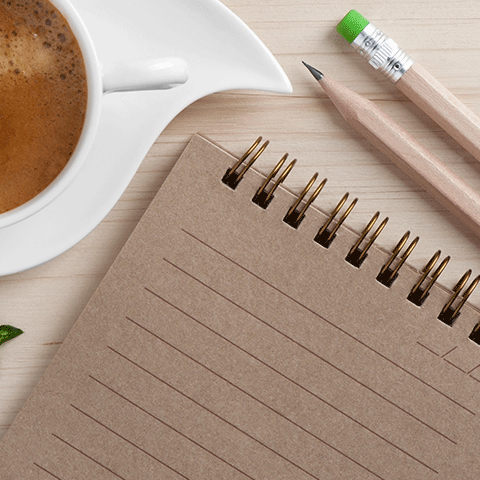 Notepad with two pencils, and a cup of coffee